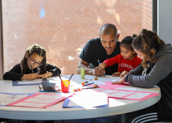 Family group seated at a round table with drawing supplies