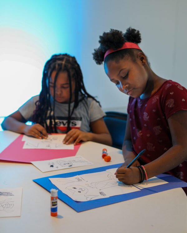 Two African American girls sitting at a table drawing