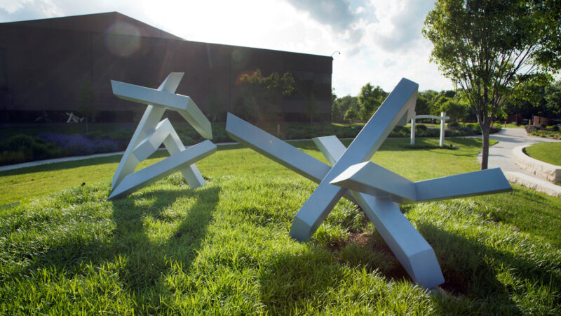 Photo of two large-scale silver abstract sculptures installed on green grass with the museum building in the background