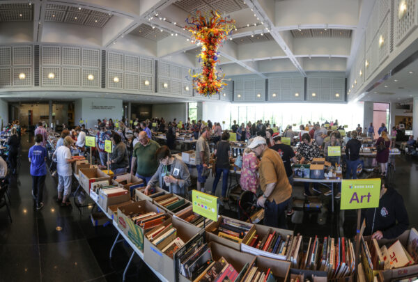 Interior photo of the Farha Great Hall with white tables set up covered with cardboard boxes full of used books being perused by dozens of museum visitors