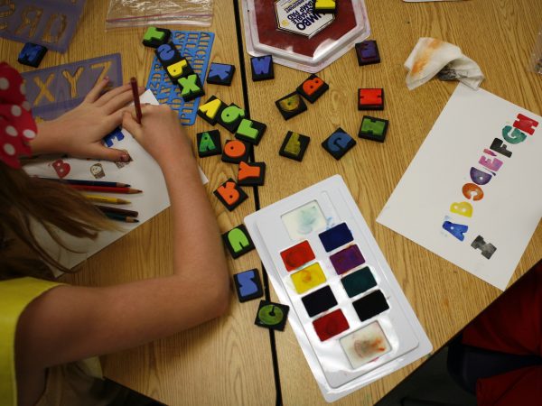Arm and hand of a child with a colorful array of paints and stamps on a table top
