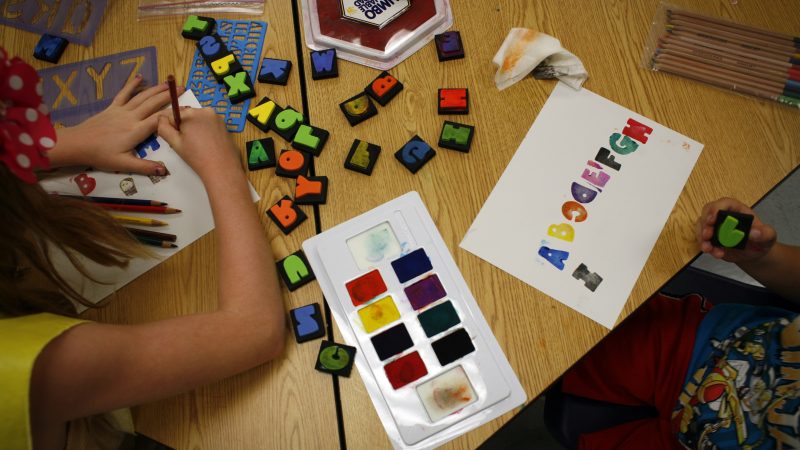 Arm and hand of a child with a colorful array of paints and stamps on a table top