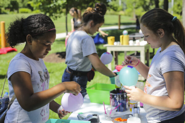 Three young girls standing at a table in the art garden with balloons and paint in the