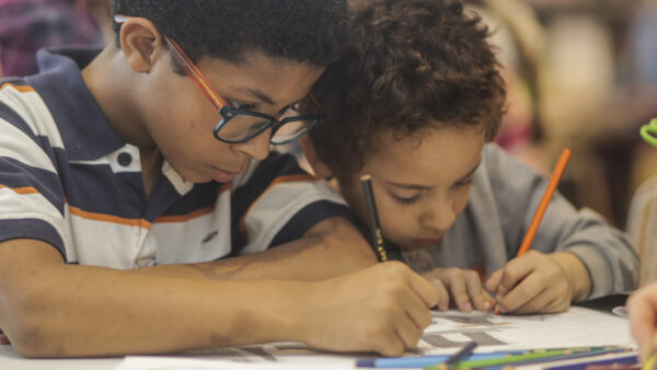 African American boys sitting at a table and drawing. Both are looking down at their drawings.