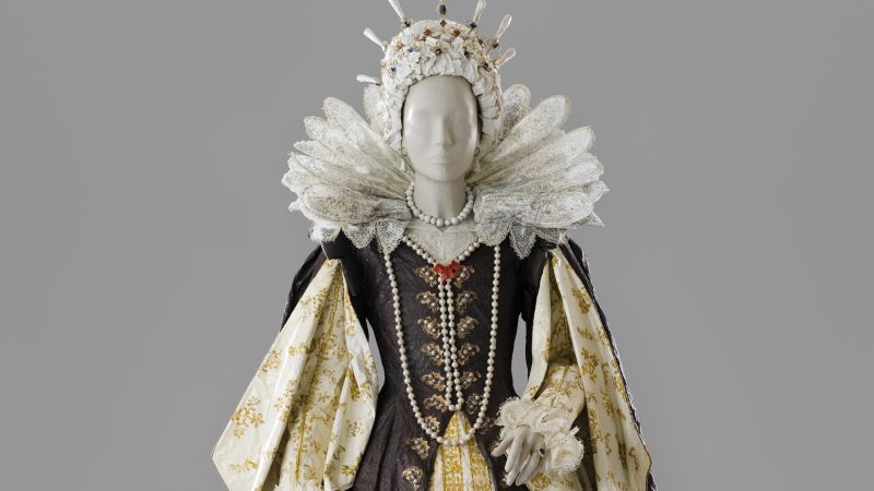 Photo of a life-size woman's royalty dress with an elaborate collar, pearls and a dress of brown and white with gold accents made entirely of paper and painted with acrylic