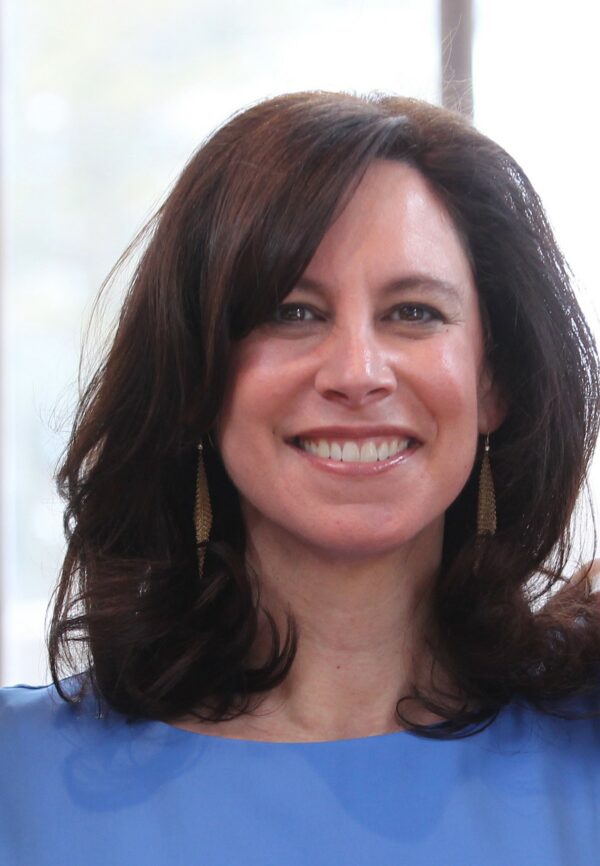 White woman pictured head and shoulders, with dark, shoulder length hair, dressed in a cornflower blue top