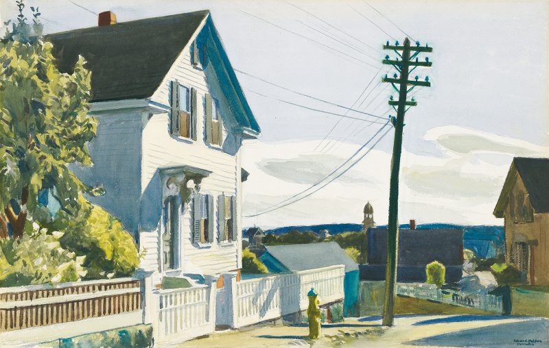 A white house seen from the street with a picket fence and utility pole to the right.