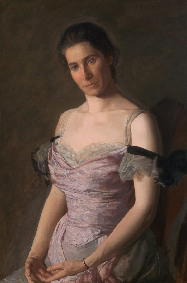 A woman sits in a pink formal gown against a dark background.