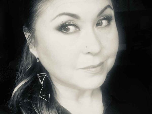 Black and white photo of a woman's face, slightly turned to the left. She has dark hair and is dressed in black