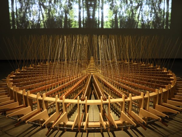 Art installation on the floor with a large, round wooden rotary shape and a video projection of a forest in the background