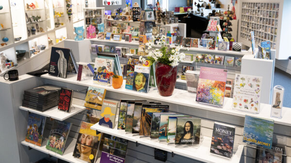 Interior view of the Museum Store showing three shelves displaying books and notecards with additional shelves of merchandise in the background