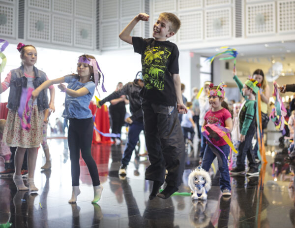 Grouo of kids dancing, boy in the foreground is jumping up with right arm raised in a fist.
