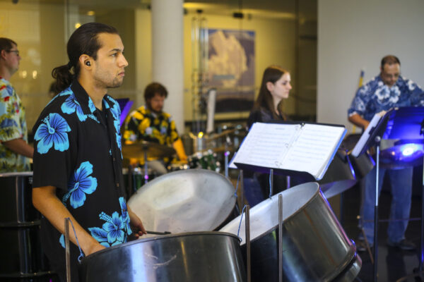 Steel Drum players, from left, man with dark hair wearing a shirt of big blue flowers on a darker blue background, other players in soft focus