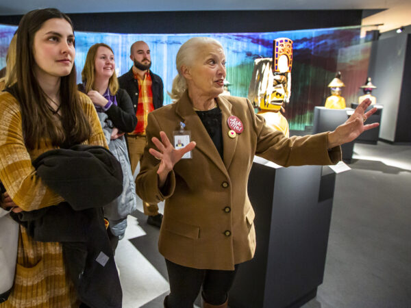 Several people in a gallery, Young woman in the foreground with long brown hair and carrying a coat. Older woman with a red 