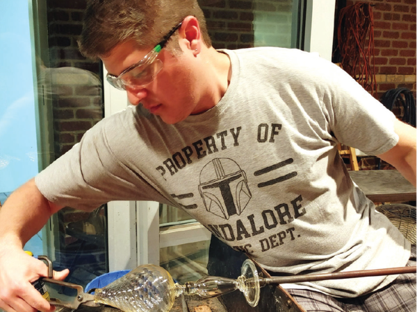 Aaron Jasso using glass blowing techniques to create a glass object.