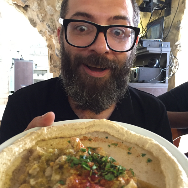 Photo for Hummus the Movie. The Host is wide-eyed, excited about showing a large plate of hummus.