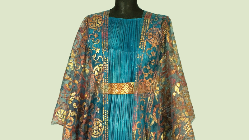 Photo of a paper dress that looks like real fabric in ruffled teal with a gold belt and a sheer gold overlay shawl with a decorative motif